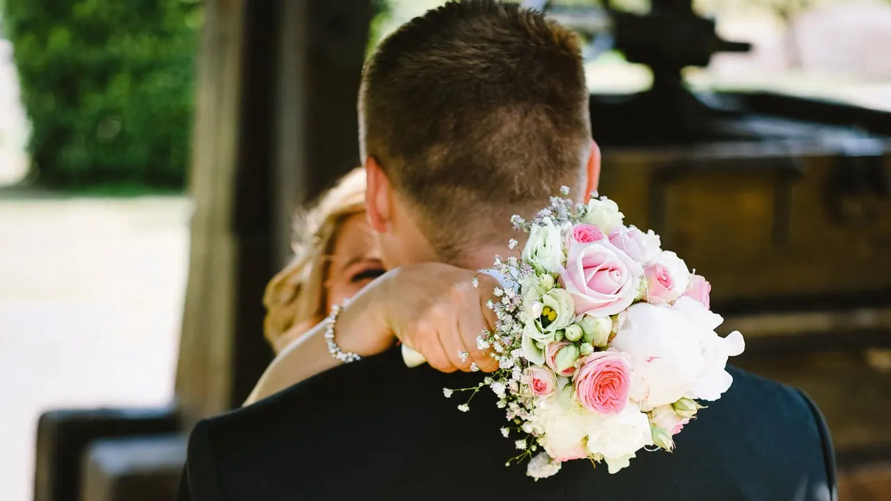 Braut umarmt den Bräutigam, in der Hand den Brautstrauß mit rosa Rosen