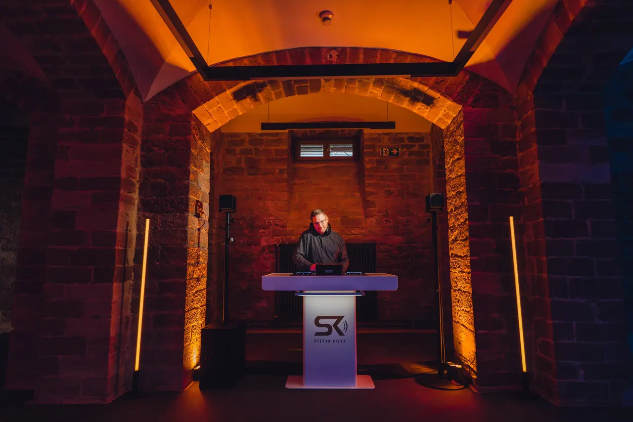 DJ-Pult mit SK-Logo im orange beleuchteten Backsteingewölbe
