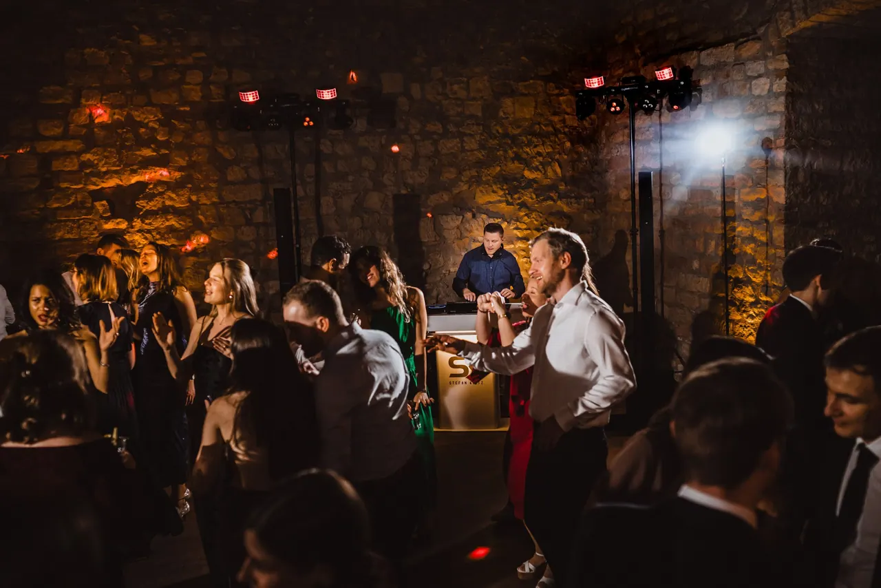 DJ am Pult in einem Gewölbe, davor feiernde Gäste