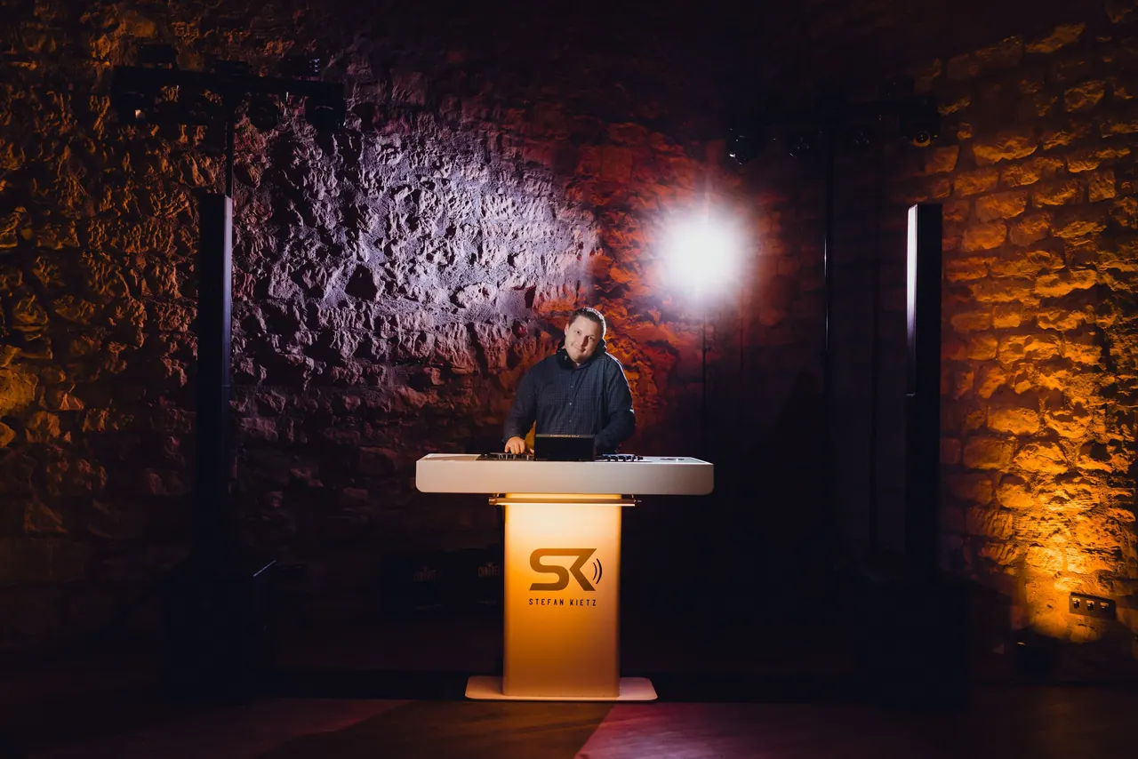 DJ-Pult mit SK-Logo vor einer warm beleuchteten Sandsteinwand