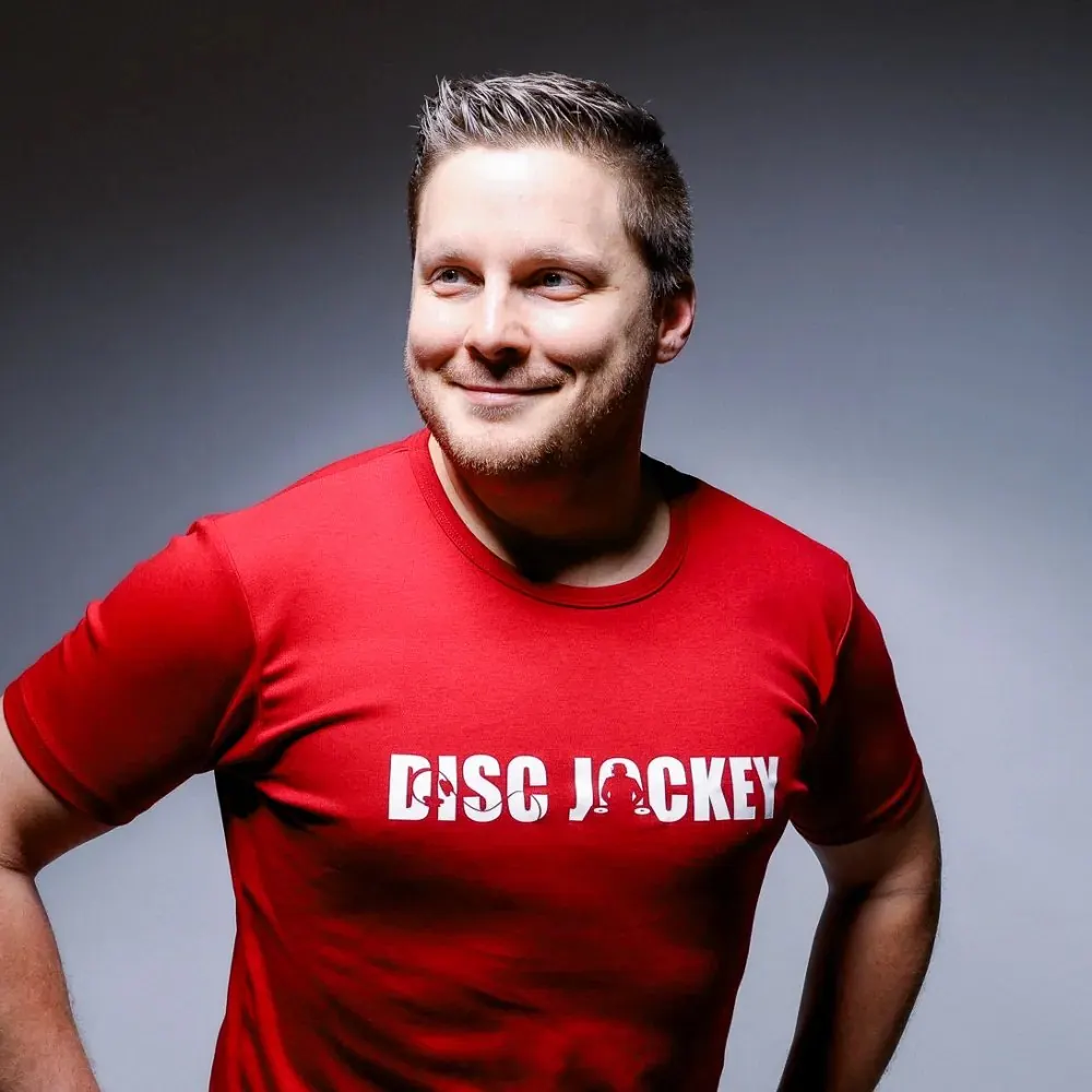Stefan Kietz lächelnd im roten T-Shirt mit der Aufschrift „Disc Jockey“