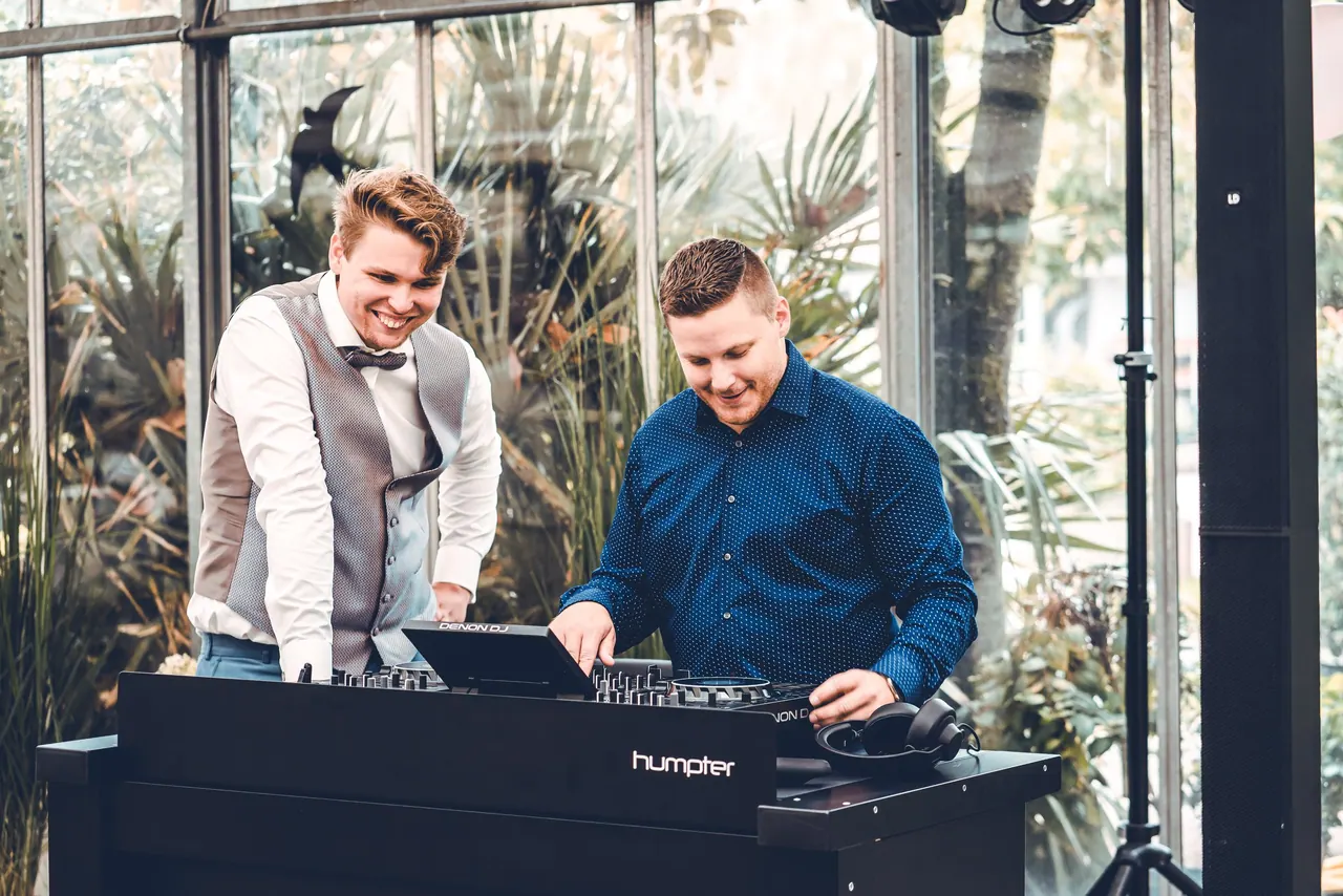 Zwei DJs lachen gemeinsam am DJ-Pult in einem Wintergarten